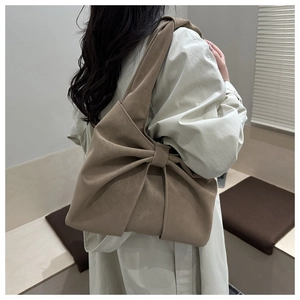 Brown bow-shaped shoulder bag shown on model wearing a classic beige trench coat