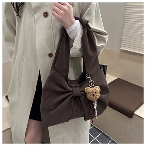 Close-up of a coffee brown suede handbag with a large bow design and a plush bear charm