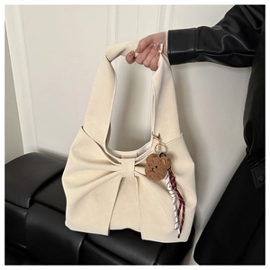 Close-up of beige tote bag featuring a large decorative bow and a plush bear charm