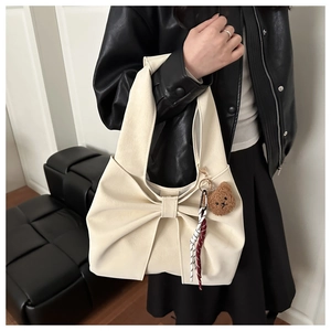 Detail of a creamy white bow tote bag with a plush bear charm and plaid ribbon accent