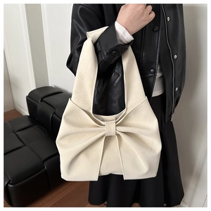 Detail of cream-colored shoulder bag featuring a large decorative bow and soft leather texture