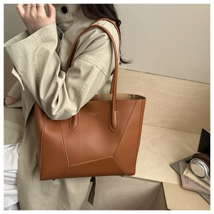 Detail shot of brown leather tote bag with metal feet on a warm wooden surface