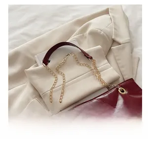 Dettaglio della borsa trapuntata bordeaux con catena d'oro su un blazer beige