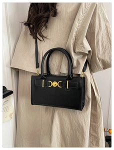 Dettaglio borsa a tracolla in pelle nera con fibbia a cuore dorata su trench beige
