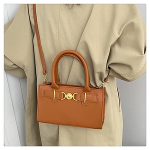 Elegante borsa tote marrone caramello con fibbia a cuore indossata su un trench beige