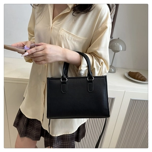 Dettaglio di una borsa nera testurizzata con strisce verticali e manici cilindrici