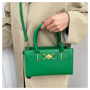 Dettaglio di una borsa in pelle verde con chiusura a cuore dorata su un trench beige