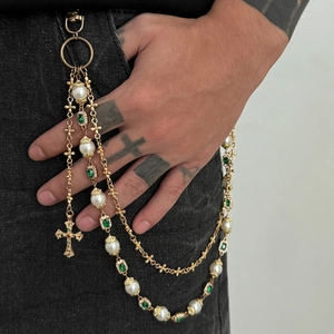 Mehrlagige goldene Hosenkette mit Perlen, grünem Zirkon und Kreuzanhänger auf Jeans