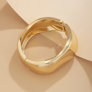 Close-up of polished gold geometric cuff bracelet with spring hinge and irregular lines