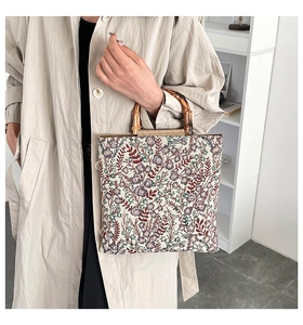 Close-up of a floral tote bag with distinctive natural bamboo handles held by a model