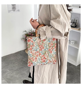 Detail of floral tote bag with vintage bamboo handles carried by a model in a trench coat