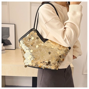Detail view of gold sequin tote bag with black strap worn by a model in interior