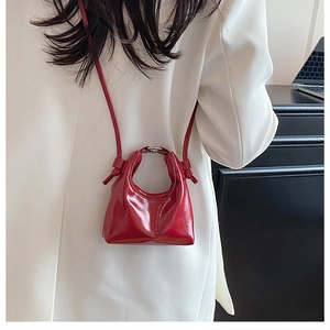 Close-up of a glossy red croissant mini bag with elegant knot detail on the shoulder strap