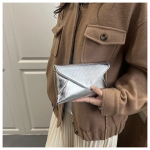 Détail du sac enveloppe argenté à texture ondulée avec chaîne dorée sur mannequin