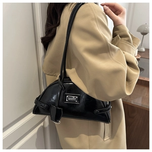 Detail of black glossy shoulder bag with silver metal plaque on beige trench coat