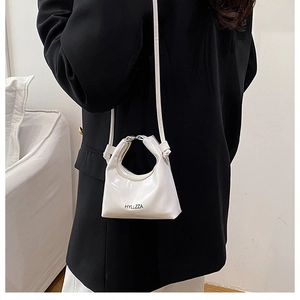 Detailed view of white patent leather bag with HYLLZZA logo on a black suit model