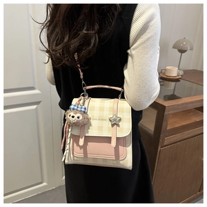 Detail of beige plaid crossbody bag with star decor and plush charm on casual outfit
