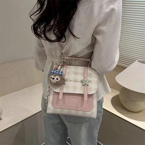 Pink plaid backpack with star buckle and plush charm worn by a model in soft light