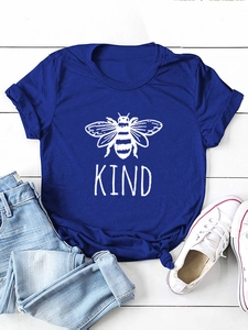 T-shirt blu reale distesa con illustrazione di ape e scritta KIND su sfondo di legno