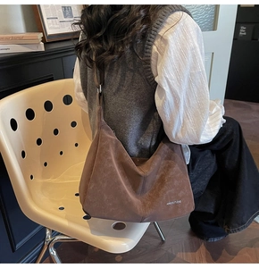 Detail of a large dark brown suede hobo bag with a minimalist logo worn on shoulder