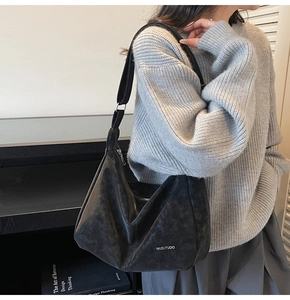 Detail of a large black faux suede hobo bag worn with a casual gray knit sweater