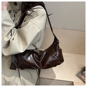Détail d'un sac hobo plissé marron foncé brillant porté avec un trench-coat beige
