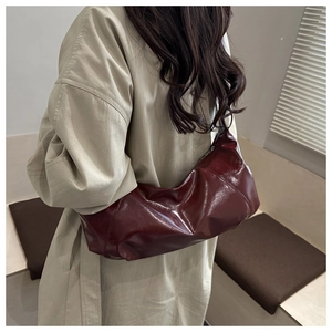 Détail du sac à bandoulière plissé brillant bordeaux porté par un mannequin en trench