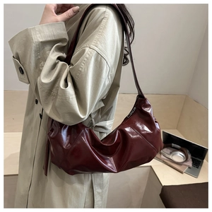 Détail du sac hobo en cuir verni bordeaux avec fermeture éclair argentée et fini brillant