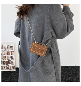 Dettaglio borsa scamosciata marrone con cuciture bianche e catena d'oro su cappotto grigio
