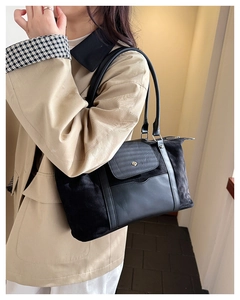Woman in beige trench coat carrying a large black shoulder travel bag for weekend trips