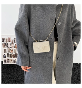 Dettaglio di una mini borsa beige chic con catena dorata indossata su un cappotto