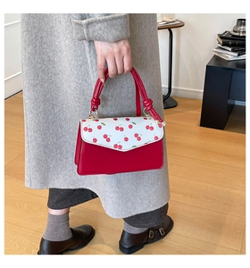 Detail of red cherry print flap and rope knot handle on a stylish square handbag