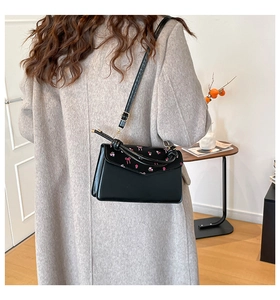 Detail of black square crossbody bag featuring floral embroidery and adjustable strap