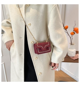 Dettaglio mini borsa a catena bordeaux con cuciture a V su cappotto in tweed crema