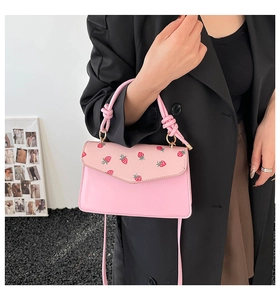 Detail of pink strawberry print handbag featuring a knotted handle and gold metal ring
