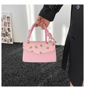 Detail of pink strawberry print handbag featuring unique knot handles and gold rings