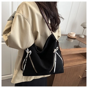 Detail of black tote bag with silver zippers, bow accents, and brown leather straps