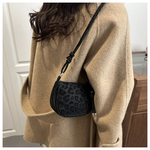Detail of leopard print crossbody bag worn over a camel wool coat in a home setting
