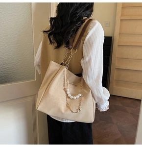 Dettaglio borsa shopper beige con catena dorata e perle bianche sulla spalla della modella