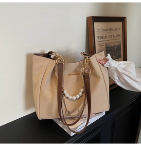 Dettaglio della borsa beige con catena di perle, finiture dorate e manici in pelle marrone