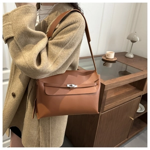 Sac bandoulière en cuir marron caramel porté sur un manteau beige avec fermoir argenté