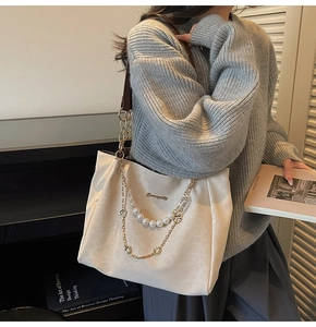 Dettaglio della borsa tote bianco crema con catena dorata e perle indossata da una modella