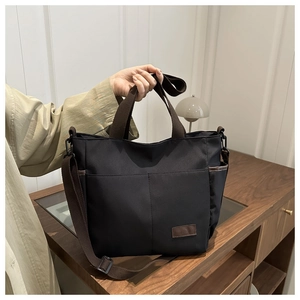 Dettaglio borsa in tela nera con manici marroni e logo in pelle per uso quotidiano
