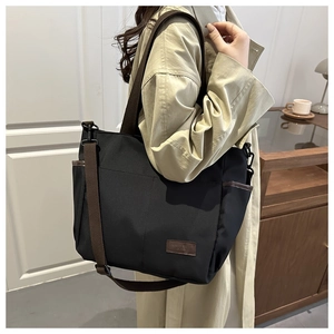Dettaglio della borsa tote in tela nera con tasca laterale e patch logo in pelle marrone