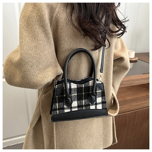Detail van vintage geruite handtas met lederen accenten gedragen op een beige wollen jas