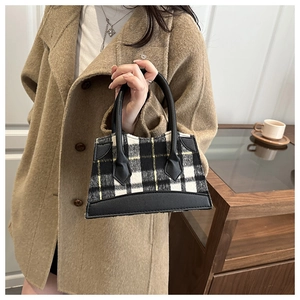 Détail d'un sac seau chic à carreaux avec garniture en cuir porté sur un manteau