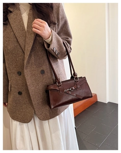 Detail of dark brown leather square bag featuring metallic buckle and eyelet strap