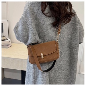 Detailed close-up of brown leather crossbody bag featuring unique gold peanut-shaped buckle