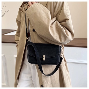 Detail of minimalist black crossbody bag with gold peanut-shaped buckle on trench coat
