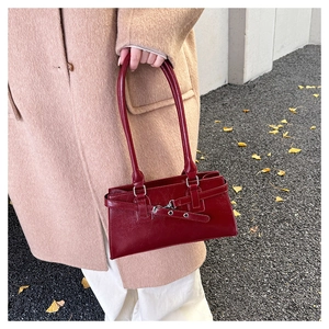 Detail einer roten glänzenden Ledertasche mit Schnallenriemen am herbstlichen Modell